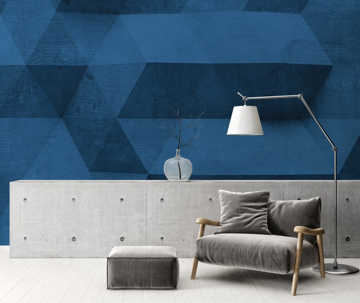 Moderne Fototapete mit blauem geometrischem 3D-Muster in Betonoptik, kombiniert mit einem Sessel, Hocker und einer hellen Sichtbetonwand.