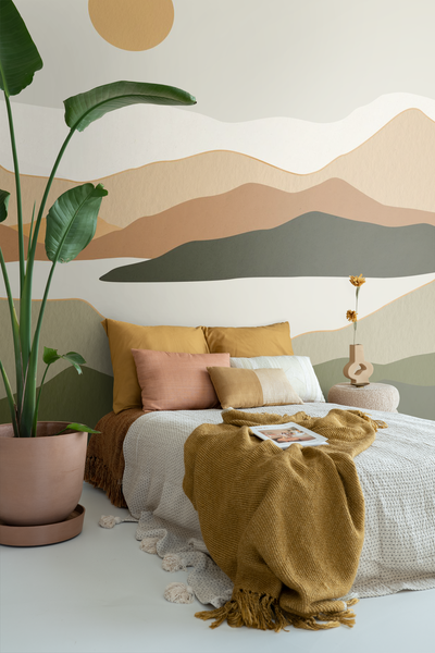 Schlafzimmer mit Bett, Kissen, Decke und Zimmerpflanze vor einer Wand mit Bergmotiv