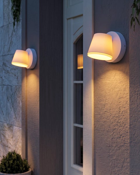 Moderne Außenwandleuchten mit konischem Schirm an einer Hauswand neben einer Tür, die warmes Licht nach unten abgeben.