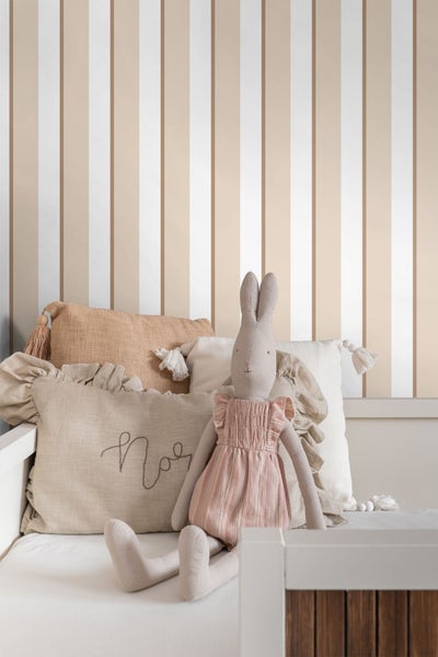 Dekorative Kissen und ein Stoffhase auf einem Kinderbett vor einer gestreiften Wand