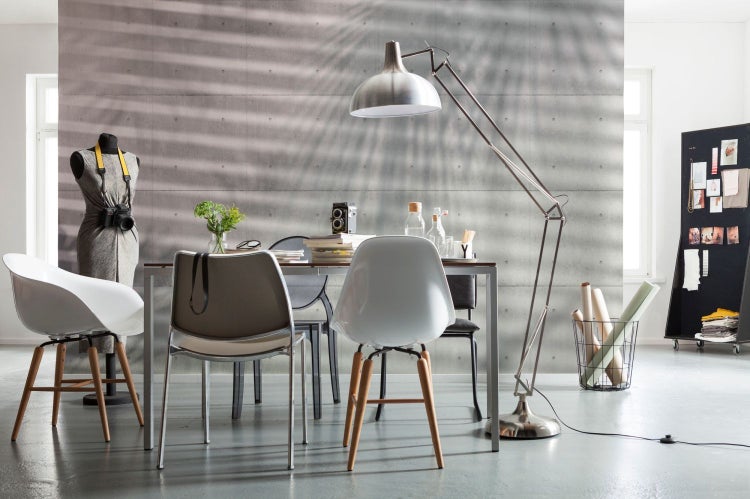 Wohnraum mit Esstisch, Stühlen, Stehlampe und Dekoration vor einer Betonwand