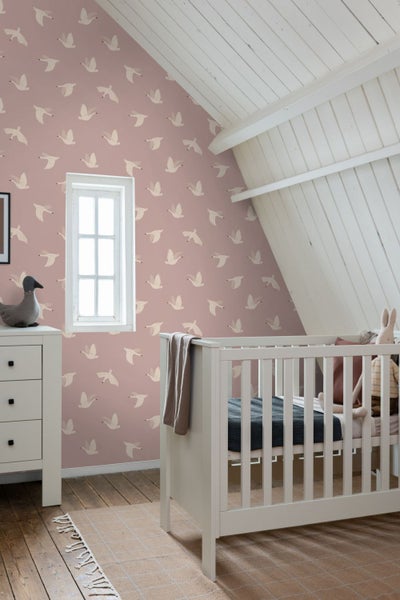 Babyzimmer mit rosa Tapete mit Vogelmuster, Gitterbett und Kommode