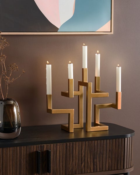Goldfarbener Kerzenständer mit fünf brennenden Kerzen auf einem Schrank.