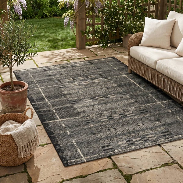 Rechteckiger Outdoor-Teppich mit geometrischem Muster auf einer Terrasse mit Sofa und Pflanzen.