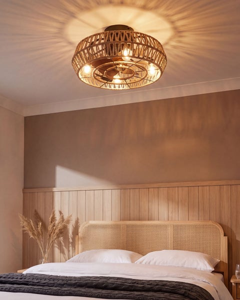Moderne Deckenleuchte mit Ventilator in Korboptik installiert an einer Schlafzimmerdecke über einem Bett mit Holzverkleidung.