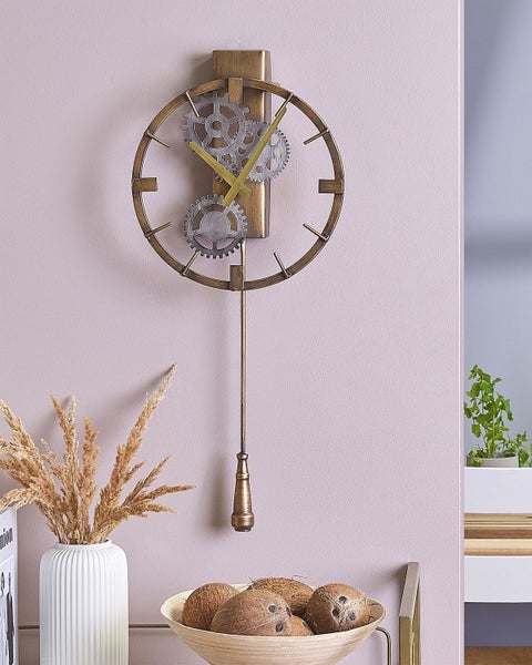 Wanduhr im industriellen Steampunk-Stil aus Metall mit sichtbaren Zahnrädern und Pendel in einem hellen Raum mit Trockenblumen.