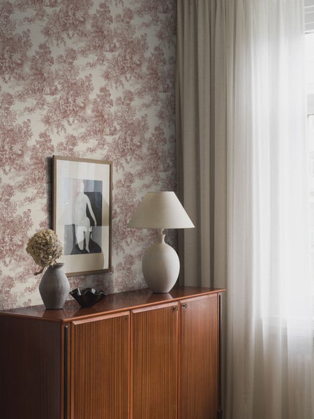 Schlafzimmer mit gemusterter Tapete, Rattan-Kopfteil und Zimmerpflanzen