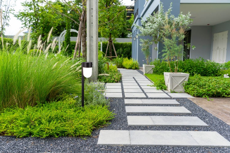 Gartenweg mit Trittplatten, Kies und Beleuchtung in einem modern gestalteten Garten.