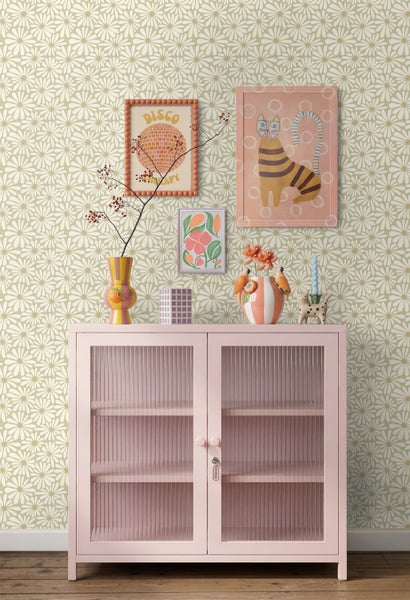 Vliestapete mit retro Gänseblümchen-Muster in hellem Zimmer. Rosa Schrank mit Glastüren, dekorative Vasen und Wandbilder.