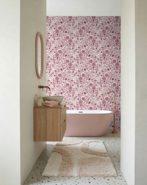 Modernes Badezimmer mit floraler Tapete, freistehender rosa Badewanne, Holzunterschrank und Terrazzoboden.