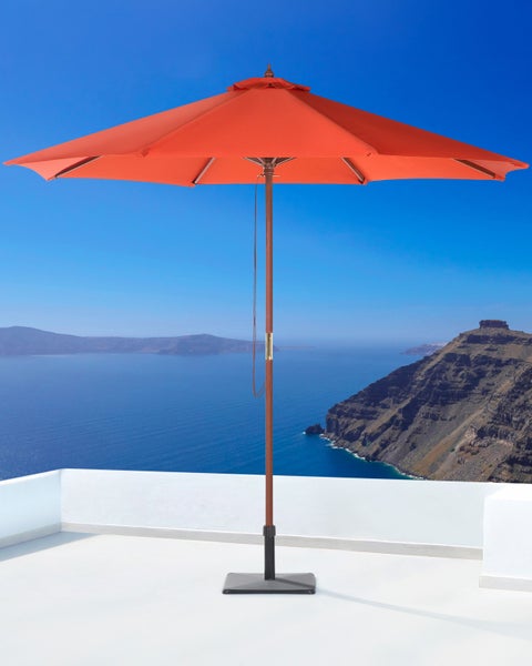 Großer oranger Sonnenschirm mit Holzmast und quadratischem Standfuß auf einer weißen Terrasse mit Meerblick.