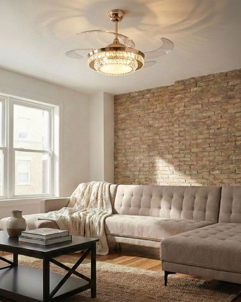 Moderner Deckenventilator mit ausfahrbaren transparenten Flügeln und Kristall-Leuchte in einem Wohnzimmer mit Backsteinwand und Sofa.
