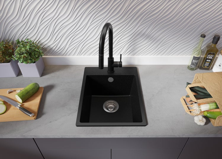 Schwarze Küchenspüle mit Armatur auf einer Arbeitsplatte mit Lebensmitteln.