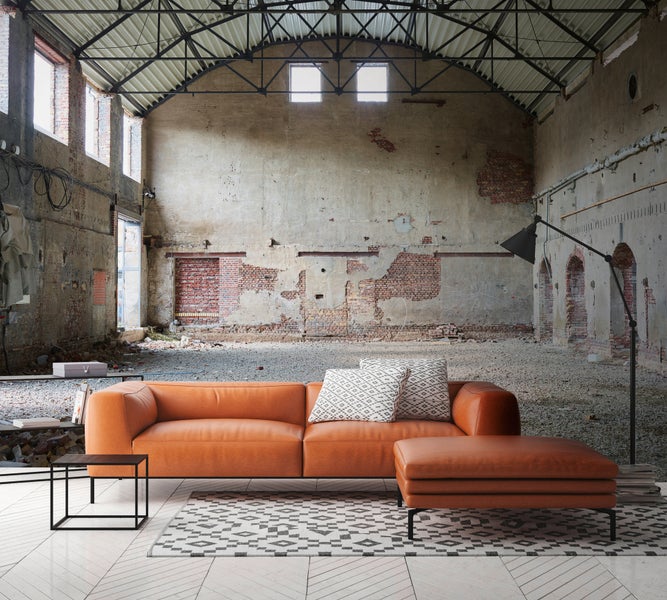 Helle Fototapete im Industriestil mit Motiv einer alten Werkshalle, Backstein und Metallträgern hinter einem modernen Ledersofa und Teppich.