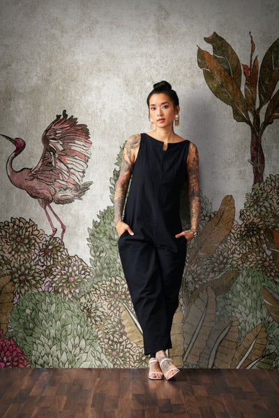 Frau in schwarzem Overall vor einer Wand mit Pflanzen- und Vogelmuster