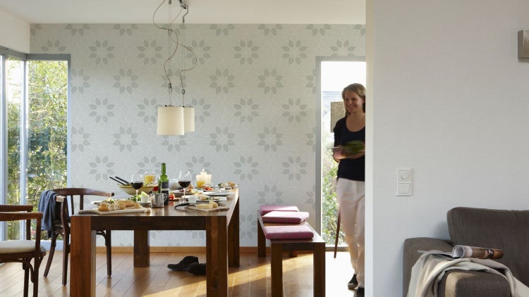 Nahaufnahme einer Wandtapete mit Blütenmuster, kombiniert mit einem Topf mit einer Pflanze und einem Buch