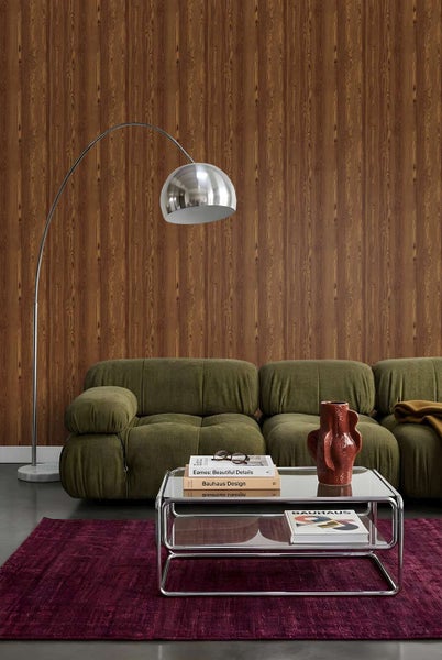 Wohnzimmer mit Vliestapete in Holzoptik, dazu ein Sofa, ein Couchtisch aus Glas und Chrom sowie eine Bogenlampe vor einer tapezierten Wand.