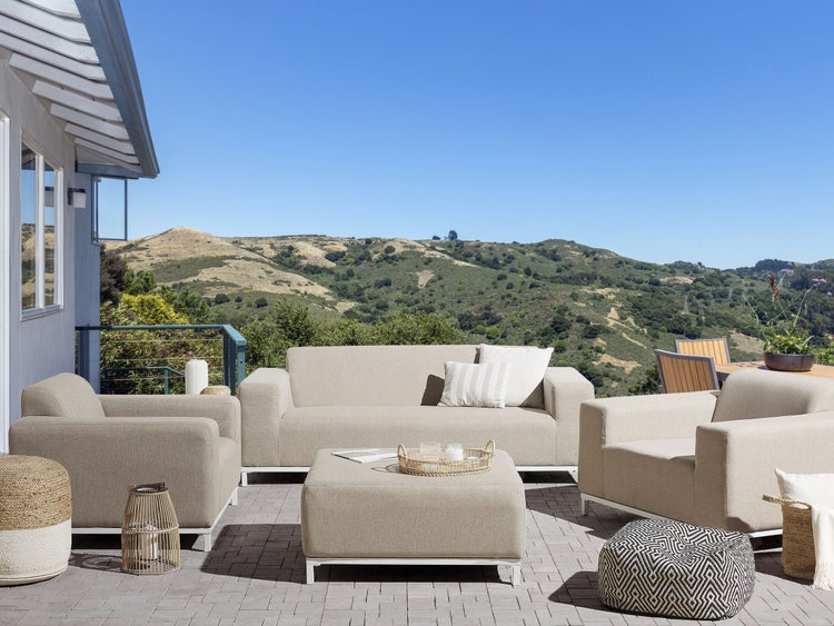 Terrasse mit Sofa, Sesseln und Hocker mit Blick auf eine grüne Hügellandschaft.