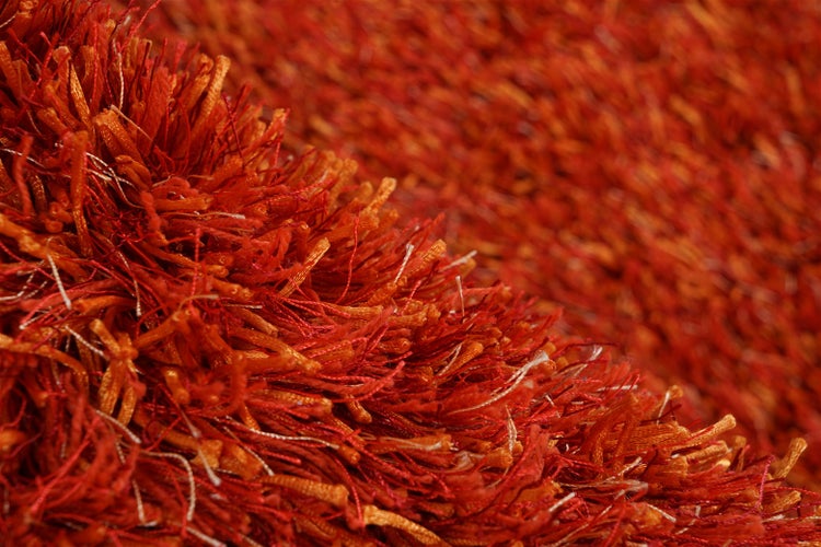 Nahaufnahme eines Hochflor-Teppichs in Rot und Orange mit dichter Zottelstruktur.