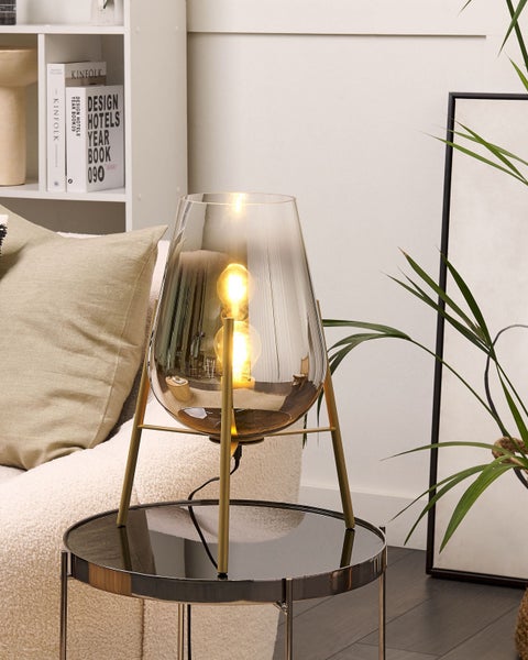 Dekorative Tischleuchte mit Glaslampenschirm und Metallgestell auf einem Beistelltisch.