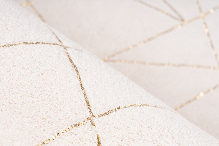 Nahaufnahme eines weichen Teppichs mit geometrischem Muster aus goldfarbenen Linien.