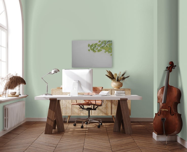 Ein helles, geräumiges Homeoffice mit einem Schreibtisch aus Holz, einem Bürostuhl aus Leder und einem Cello vor einer hellgrün gestrichenen Wand.