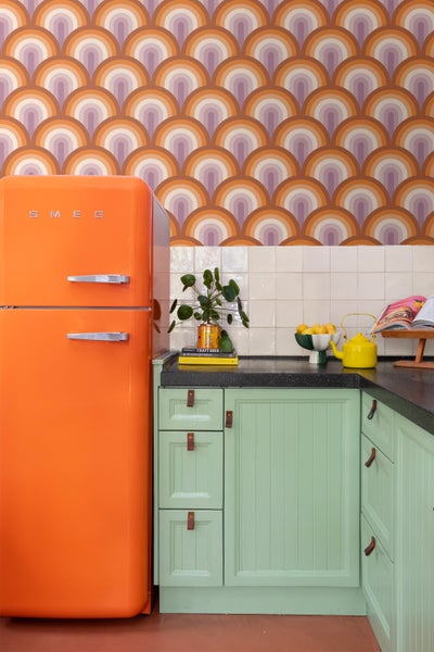 Küchenszene mit orangefarbenem Smeg Kühlschrank, mintgrünen Schränken und Retro-Tapete