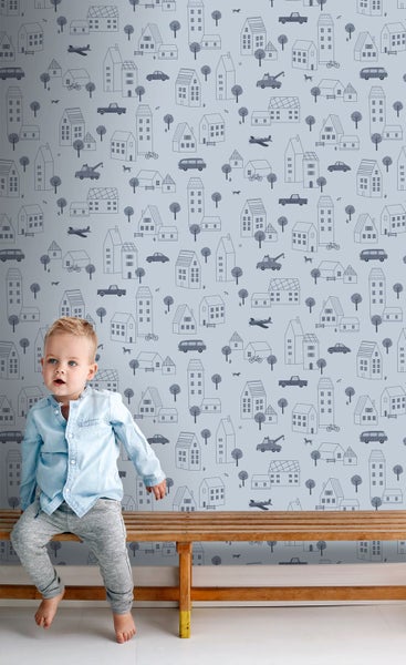 Kind sitzt vor Tapete mit Häuser Muster