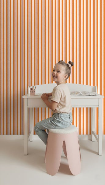 Kind sitzt an Schreibtisch vor gestreifter Tapete im Kinderzimmer