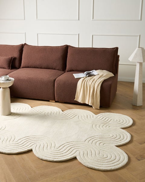 Modernes Wohnzimmer mit braunem strukturiertem Sofa, gewelltem cremefarbenem Teppich mit Wellenmuster, Stehlampe und Beistelltisch auf Parkett.