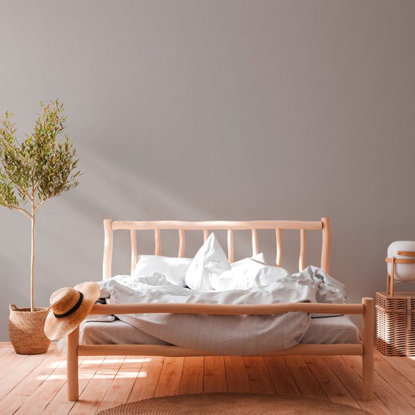 Helles Schlafzimmer mit Holzbett, Bettwäsche, geflochtener Aufbewahrung, Dekoration und Zimmerpflanze