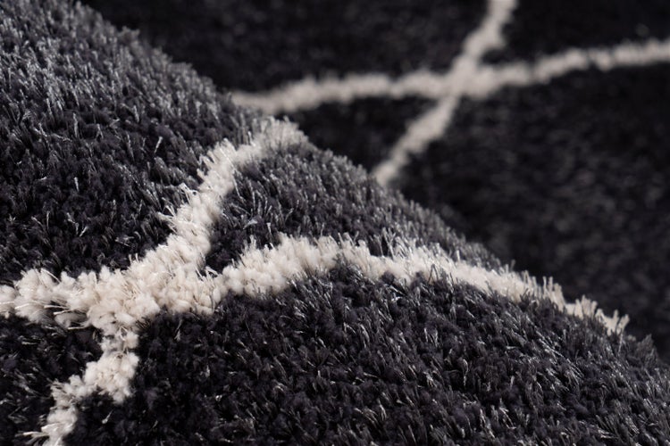 Detailansicht eines weichen Hochflor-Teppichs in Anthrazit mit weißem geometrischem Linienmuster.