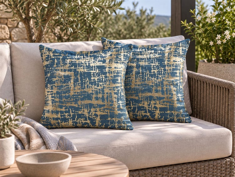 Zwei quadratische Dekokissen mit abstrakter Textilstruktur auf einem Loungesofa in einem Außenbereich mit Pflanzen
