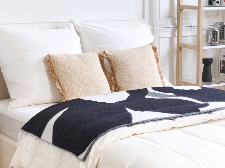 Dekoriertes Bett mit Kissen, Tagesdecke und Regal