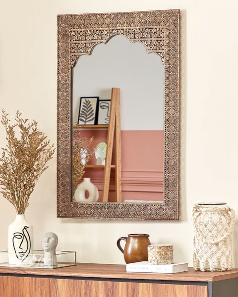 Dekoratives Interieur mit einem Spiegel mit geschnitztem Holzrahmen über einem Sideboard.