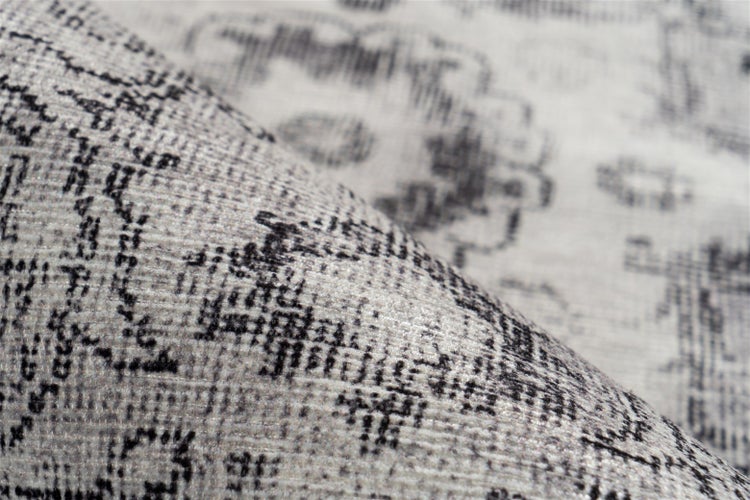 Nahaufnahme eines grau-schwarzen Teppichs mit ornamentalem Vintage-Muster und weicher gewebter Oberfläche.