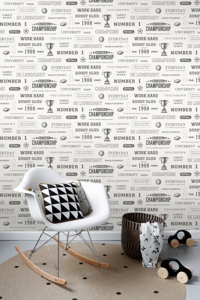 Zimmerszene mit Schaukelstuhl, Kissen, geflochtenem Korb, Spielzeugautos und Tapete mit Sportmotiven