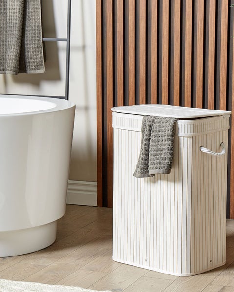 Wäschesammler aus Bambus mit Deckel und Seilgriffen in einem modernen Badezimmer neben einer Badewanne und Holzlamellenwand.