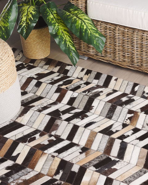 Teppich mit Zickzackmuster aus Lederstücken, kombiniert mit einer Korbcouch, einem Hocker und einer Zimmerpflanze.