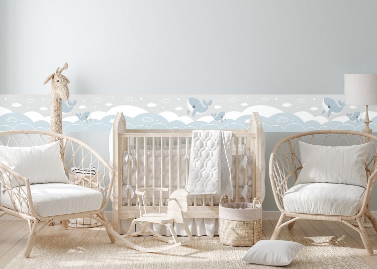 Selbstklebende Tapetenbordüre für das Kinderzimmer mit Wal-, Wolken- und Sternenmotiv in einem hellen Babyzimmer mit Holzmöbeln.