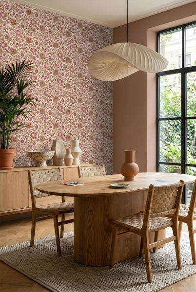 Helles Esszimmer mit floral gemusterter Vliestapete, ovalem Holztisch, geflochtenen Stühlen, einer großen Hängeleuchte und einem Sideboard.
