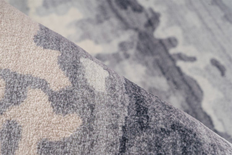 Nahaufnahme eines weichen Teppichs mit grauem und cremefarbenem abstraktem Muster.