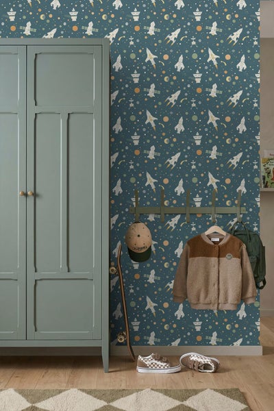 Vliestapete mit Weltraum-Motiv zeigt Raketen und Planeten in einem organisierten Kinderzimmer mit Kleiderschrank, Skateboard und Wandhaken.