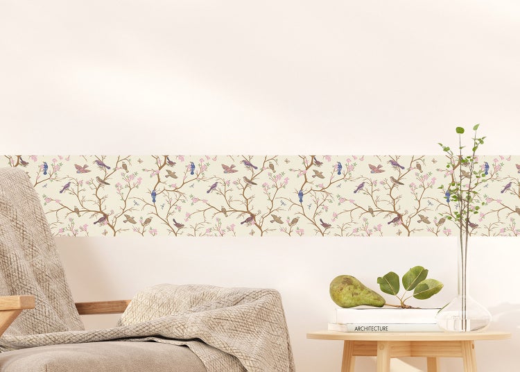 Dekorative Tapetenbordüre mit Vogel- und Astmotiv an einer hellen Wand in einem Wohnzimmer mit Sessel, grauer Decke und Beistelltisch.