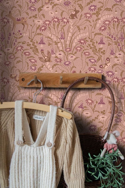 Kinderzimmertapete mit Waldtieren und Wiesenblumen, neben einem Holzregal mit Spielzeug und Kinderkleidung an einer Hakenleiste.