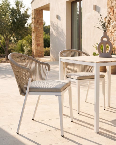 Gartenmöbel Set aus Stühlen mit Seilgeflecht und Tisch mit einer Vase auf einer Terrasse vor einer Hauswand