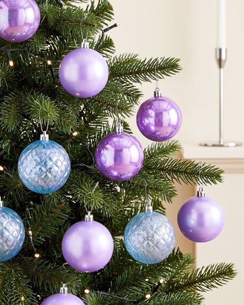 Weihnachtskugeln in verschiedenen Ausführungen hängen an einem künstlichen Tannenbaum mit Beleuchtung