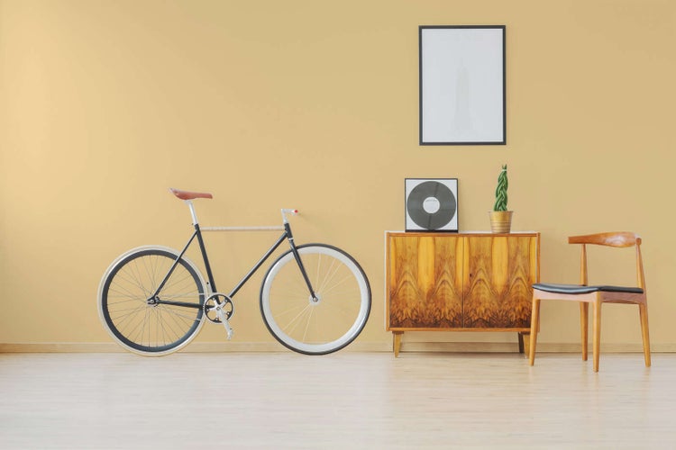 Moderner, heller Wohnraum mit gestrichener Wand, schwarzem Fahrrad, hölzernem Sideboard und Designerstuhl auf Holzboden.