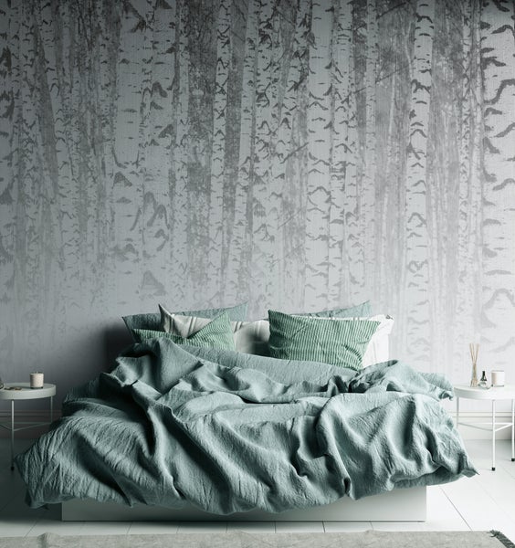Fototapete mit Birkenwald-Motiv hinter einem Bett mit grüner Bettwäsche und zwei weißen Beistelltischen in einem hellen Schlafzimmer.