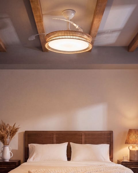 Deckenventilator mit Beleuchtung und Rattanoptik installiert an einer Zimmerdecke über einem Schlafzimmerbett im natürlichen Einrichtungsstil.